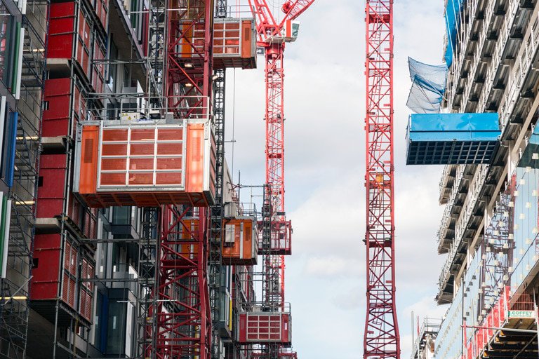 Alimak construction hoists at a large high-rise building site with tower cranes